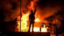 TOPSHOT - A protester reacts standing in front of a burning building set on fire during a demonstration in Minneapolis, Minnesota, on May 29, 2020, over the death of George Floyd, a black man who died after a white policeman kneeled on his neck for several minutes. Violent protests erupted across the United States late on May 29 over the death of a handcuffed black man in police custody, with murder charges laid against the arresting Minneapolis officer failing to quell seething anger. (Photo by Chandan KHANNA / AFP) (Photo by CHANDAN KHANNA/AFP via Getty Images)